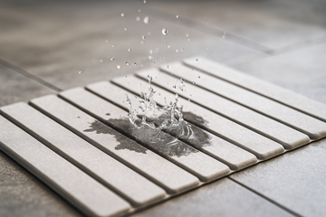 Close-up shot of water drops instantly disappearing into the surface of a sleek, modern diatomaceous earth stone bath mat, highlighting its rapid absorption