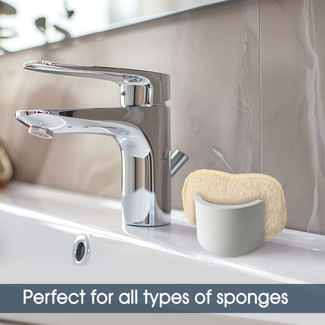 Chrome faucet on a sink with a sponge holder and sponge, against a neutral tiled wall.