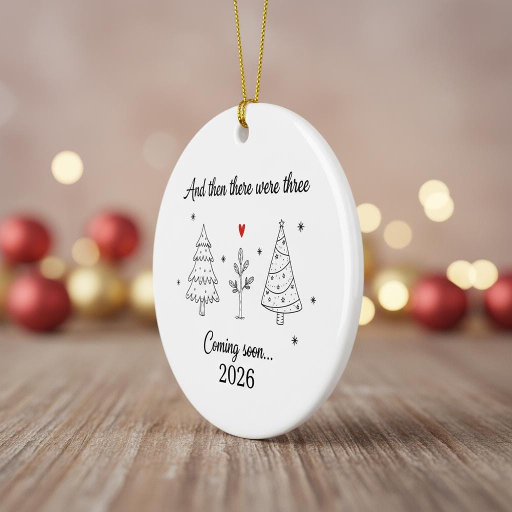 White ceramic ornament with Christmas tree designs and text on a wooden surface with blurred lights in the background