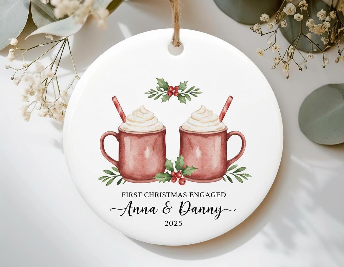 Decorative ornament with two mugs of hot chocolate, Christmas decorations, and text 'First Christmas Engaged Anna & Danny 2023' on a white background.