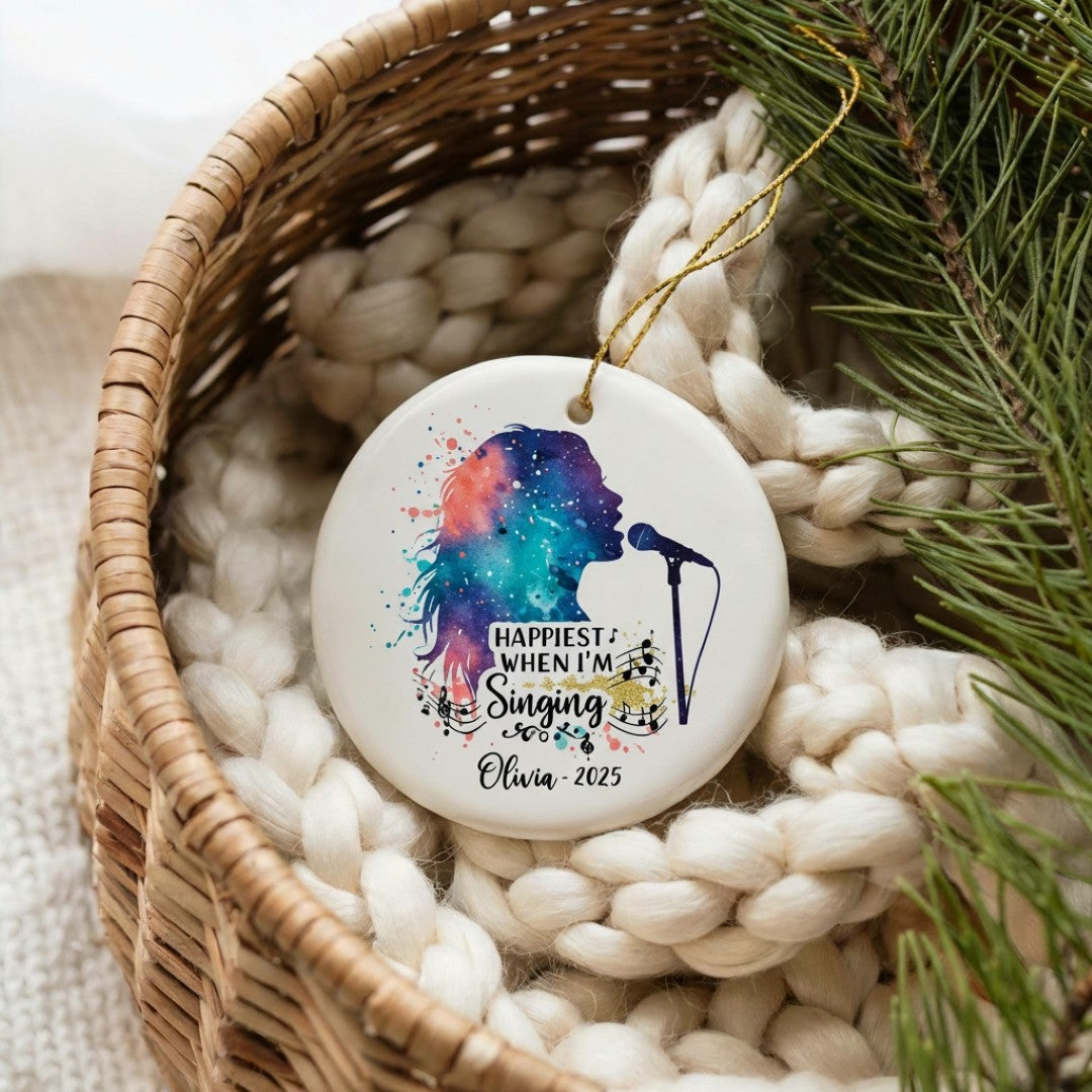 Decorative ornament with colorful silhouette and text, placed in a woven basket with white stones and greenery.