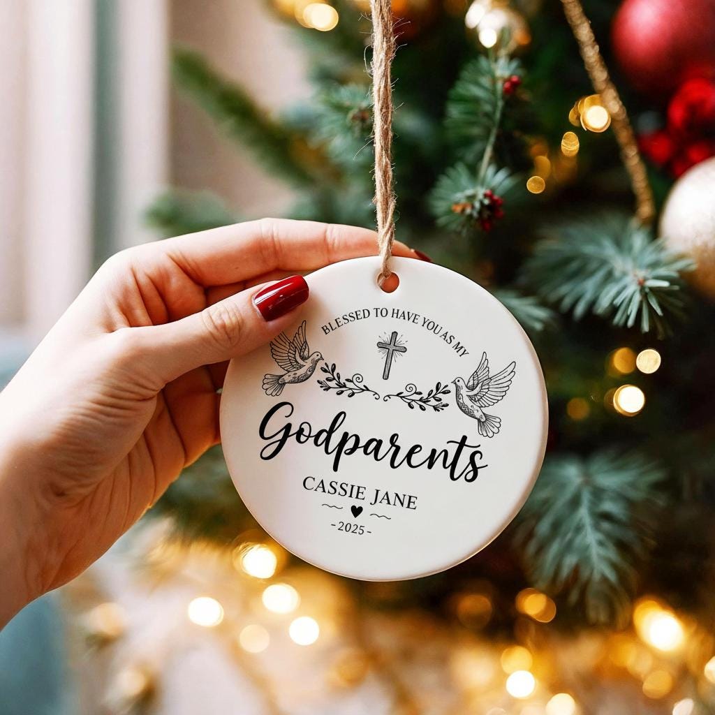 Round ornament with 'Godparents' text held in front of a Christmas tree.