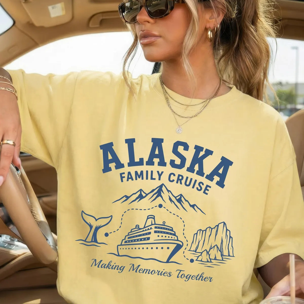 Woman in sunglasses and a Butter yellow Comfort Colors tee in a car, navy Alaska Family Cruise above a whale tail and ship