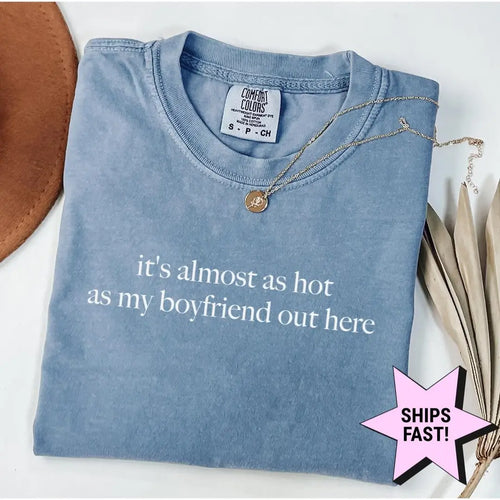 Folded Blue Jean Comfort Colors tee with the two-line almost as hot as my boyfriend quote in white serif, brown hat nearby