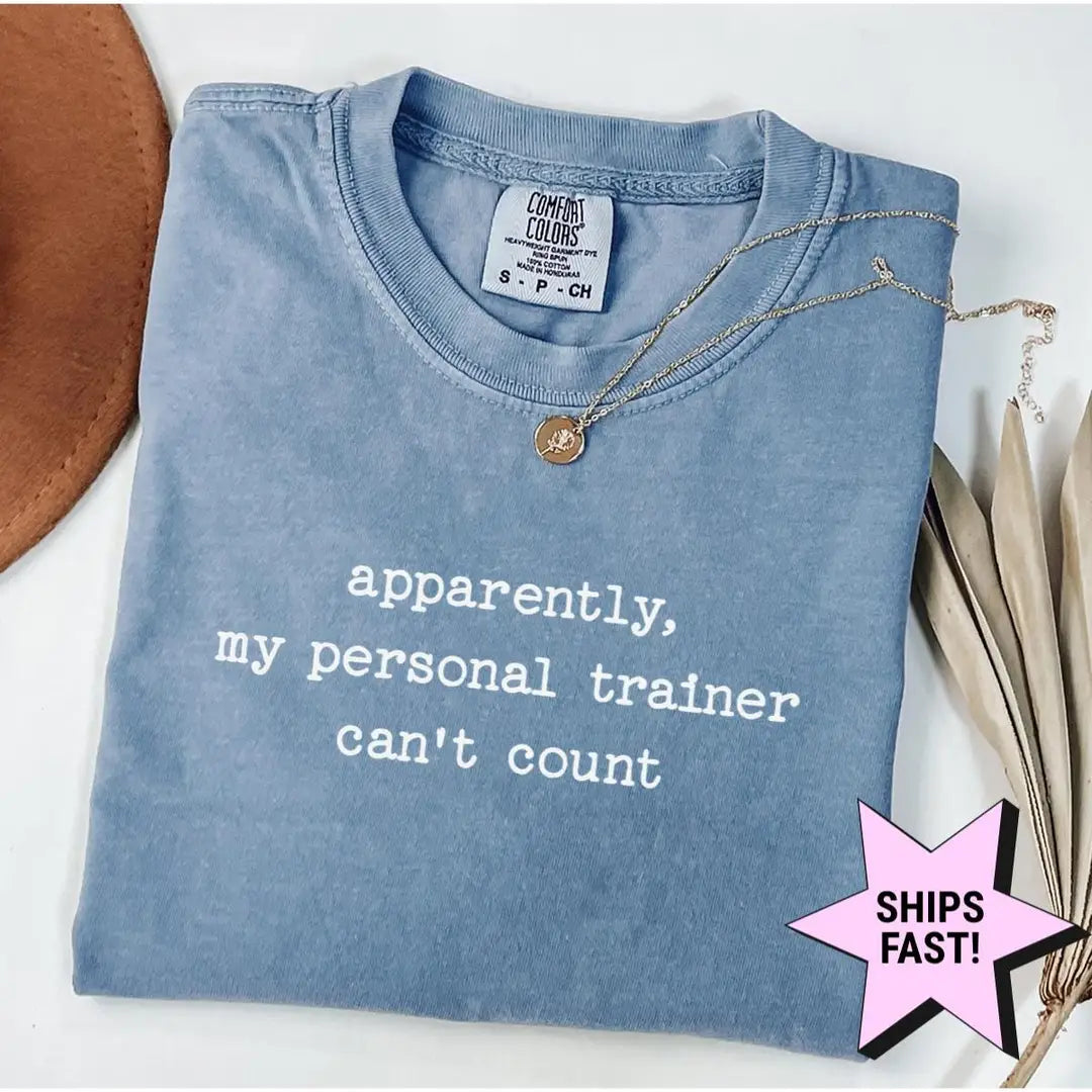 Folded Blue Jean Comfort Colors tee with apparently, my personal trainer can't count in white type, necklace at the collar