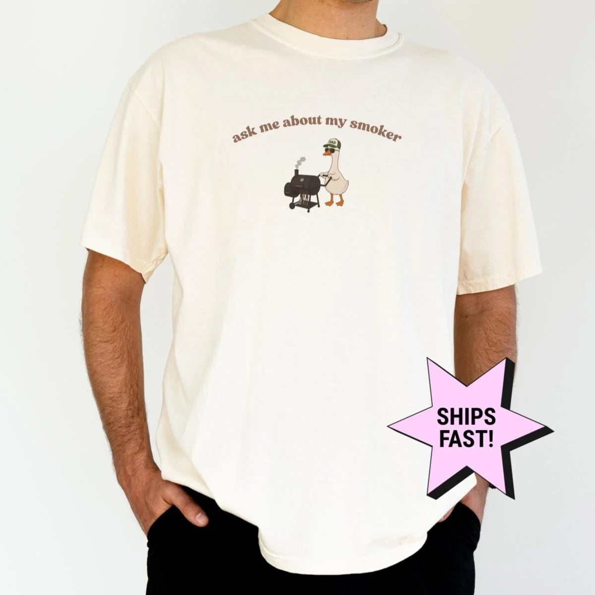 Man in an Ivory Comfort Colors tee with a goose at a smoker grill under arched ask me about my smoker lettering