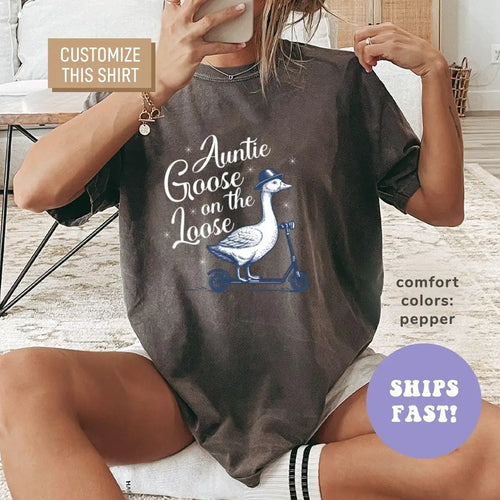 Woman in a Pepper Comfort Colors tee taking a mirror selfie, an Auntie Goose on the Loose print with a goose on a scooter