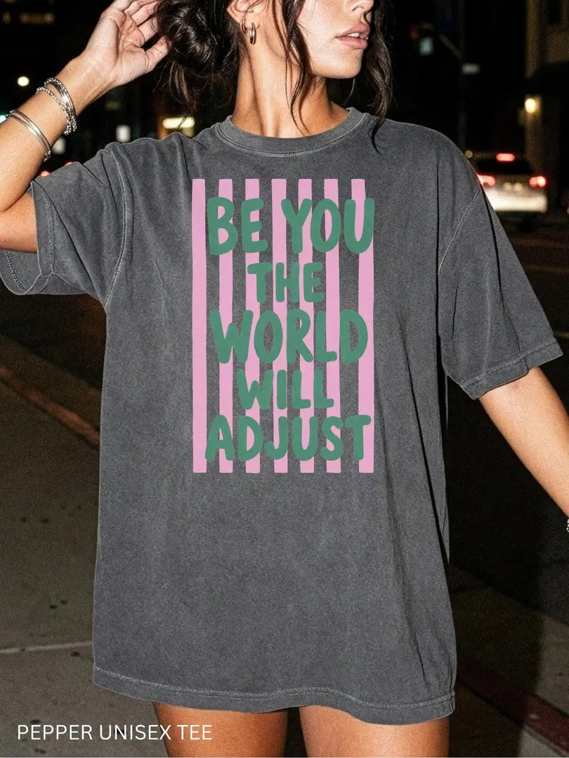 Woman in a Pepper Comfort Colors tee on a night street with green be you the world will adjust on pink stripes