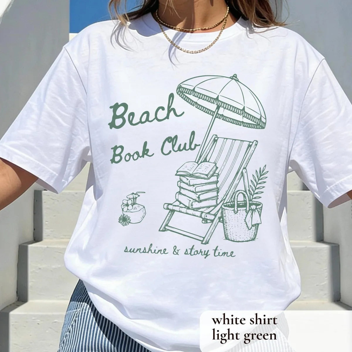Woman in a White Comfort Colors tee on white steps, sage green beach book club, lounge chair, books and coconut drink