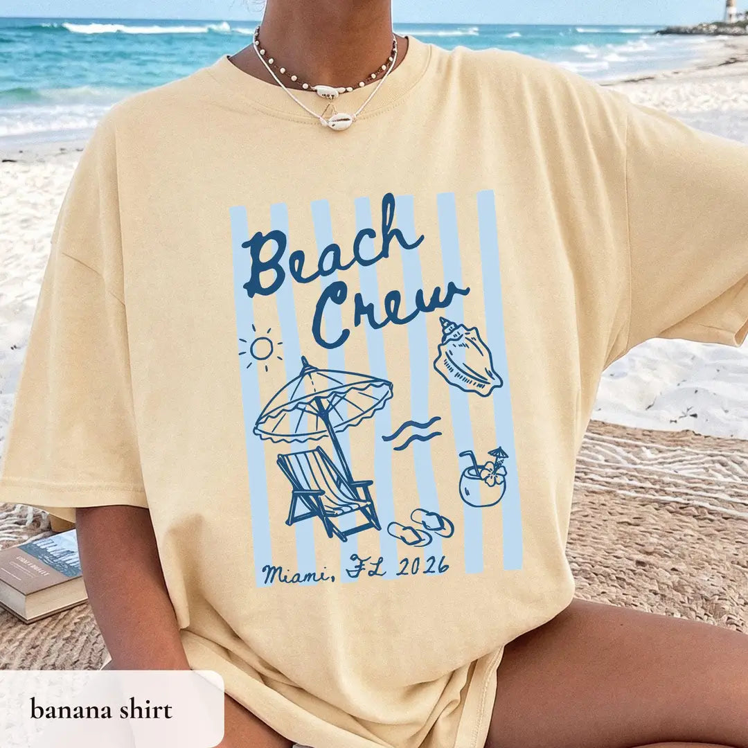 Woman in a Banana yellow Comfort Colors tee on the sand, navy beach crew lettering on blue stripes with a drink