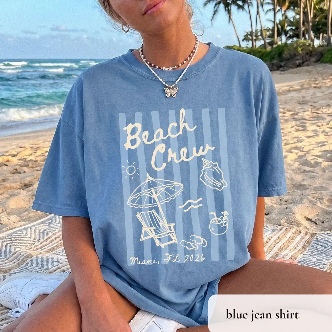 Blue Jean Comfort Colors tee with a butterfly necklace, ivory beach crew lettering, a sun, lounge chair and Miami, FL 2026