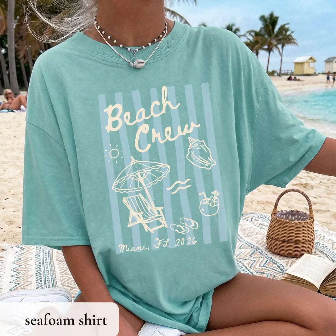 Woman in a Seafoam teal Comfort Colors tee by a wicker basket, ivory beach crew over stripes with a lounge chair