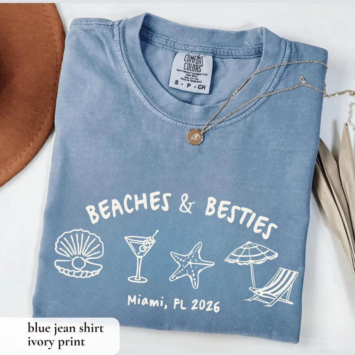 Folded Blue Jean Comfort Colors tee with white arched beaches and besties over a shell, martini, starfish and lounge chair
