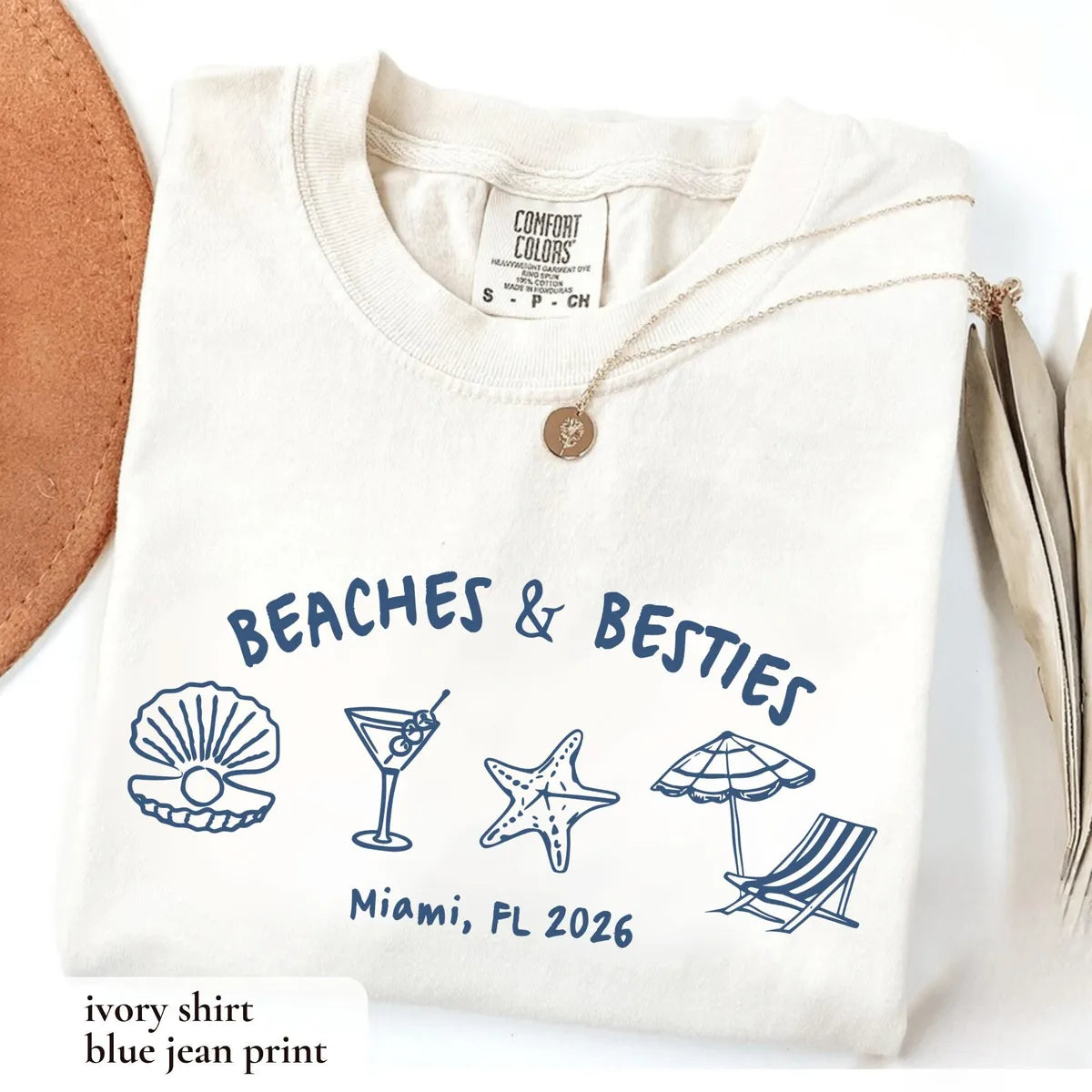 Folded Ivory Comfort Colors tee with navy blue arched beaches and besties, beach icons and a Miami, FL 2026 line