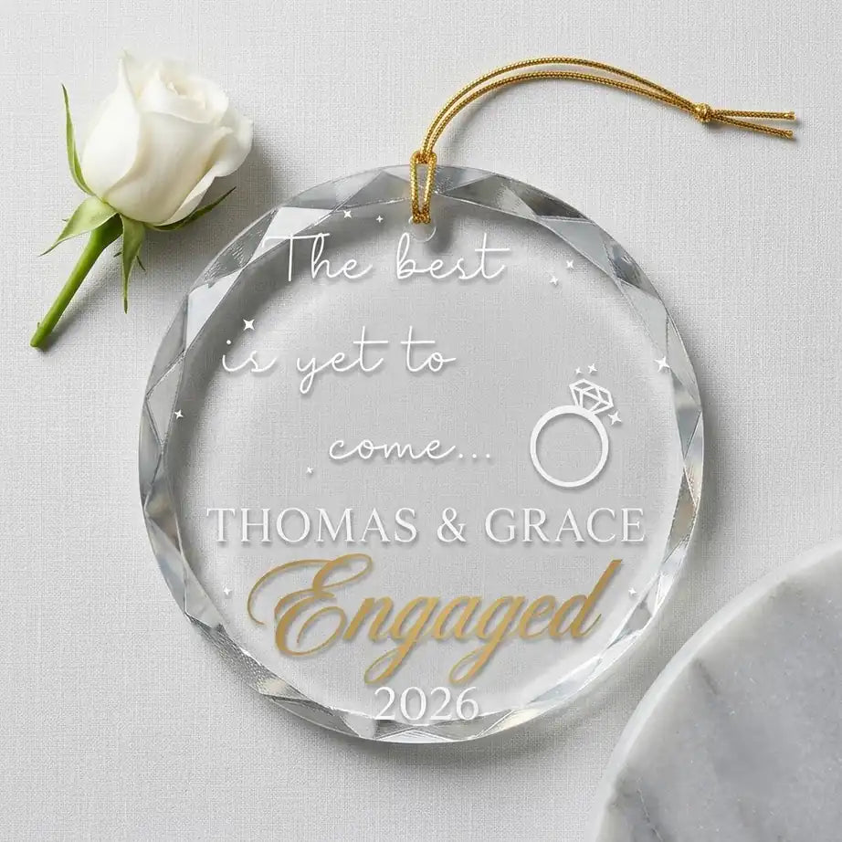 Clear glass round ornament laid flat on festive wooden surface with pine branches, pinecones and holiday decorations surrounding the engagement design