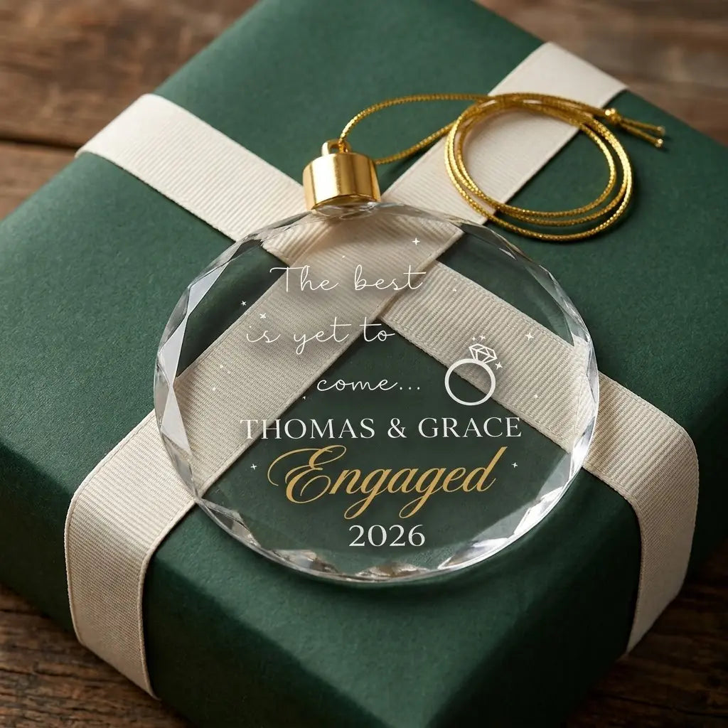 Personalized engagement glass ornament presented beside a wrapped holiday gift box on rustic wooden background