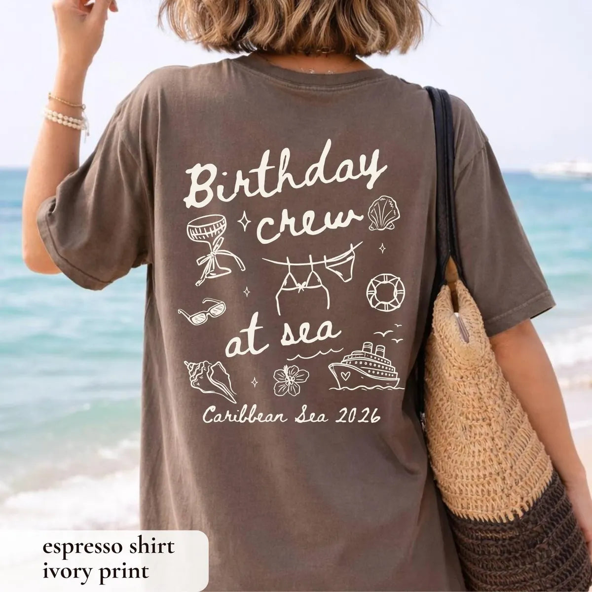 Woman in an Espresso Comfort Colors tee seen from behind with a straw tote, Birthday crew at sea in ivory, beach behind