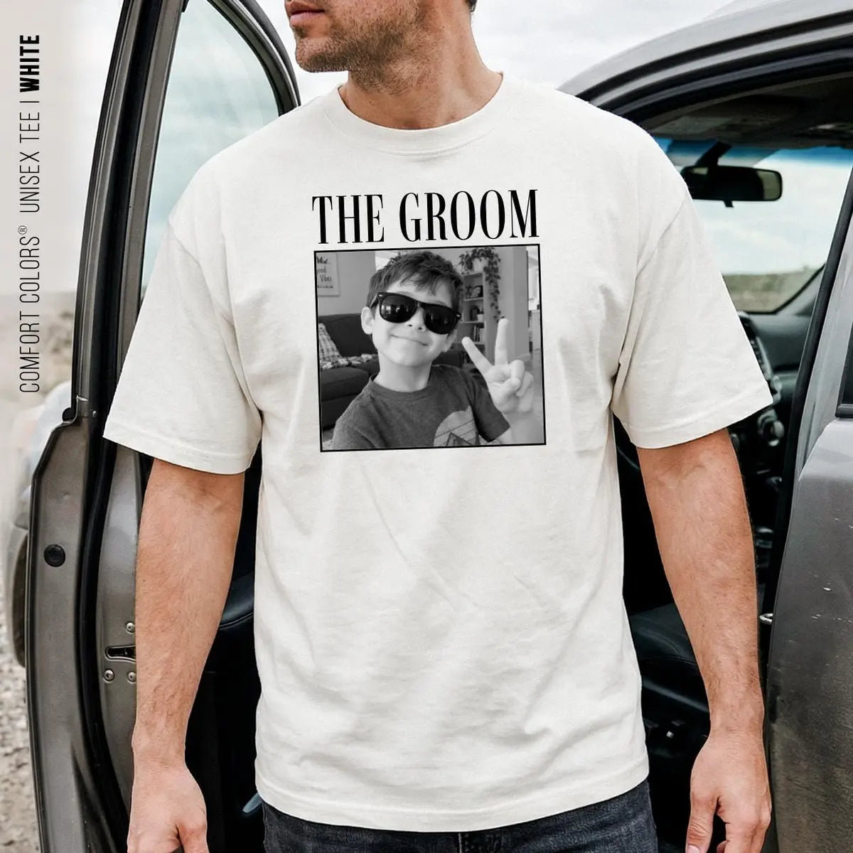 Man in a cream Comfort Colors tee stepping out of a car, the groom in serif capitals above a framed black and white photo