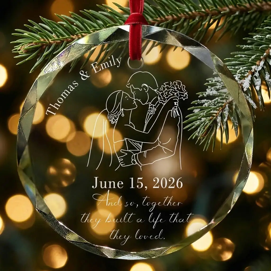 Personalized clear glass wedding anniversary ornament displayed hanging on Christmas tree branch with warm sparkling holiday lights background