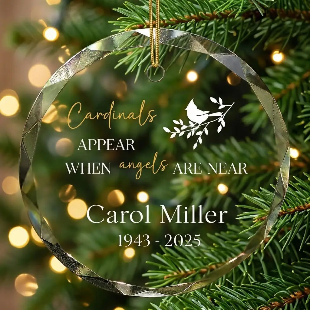 Personalized clear glass memorial remembrance ornament displayed hanging on Christmas tree branch with warm sparkling holiday lights background