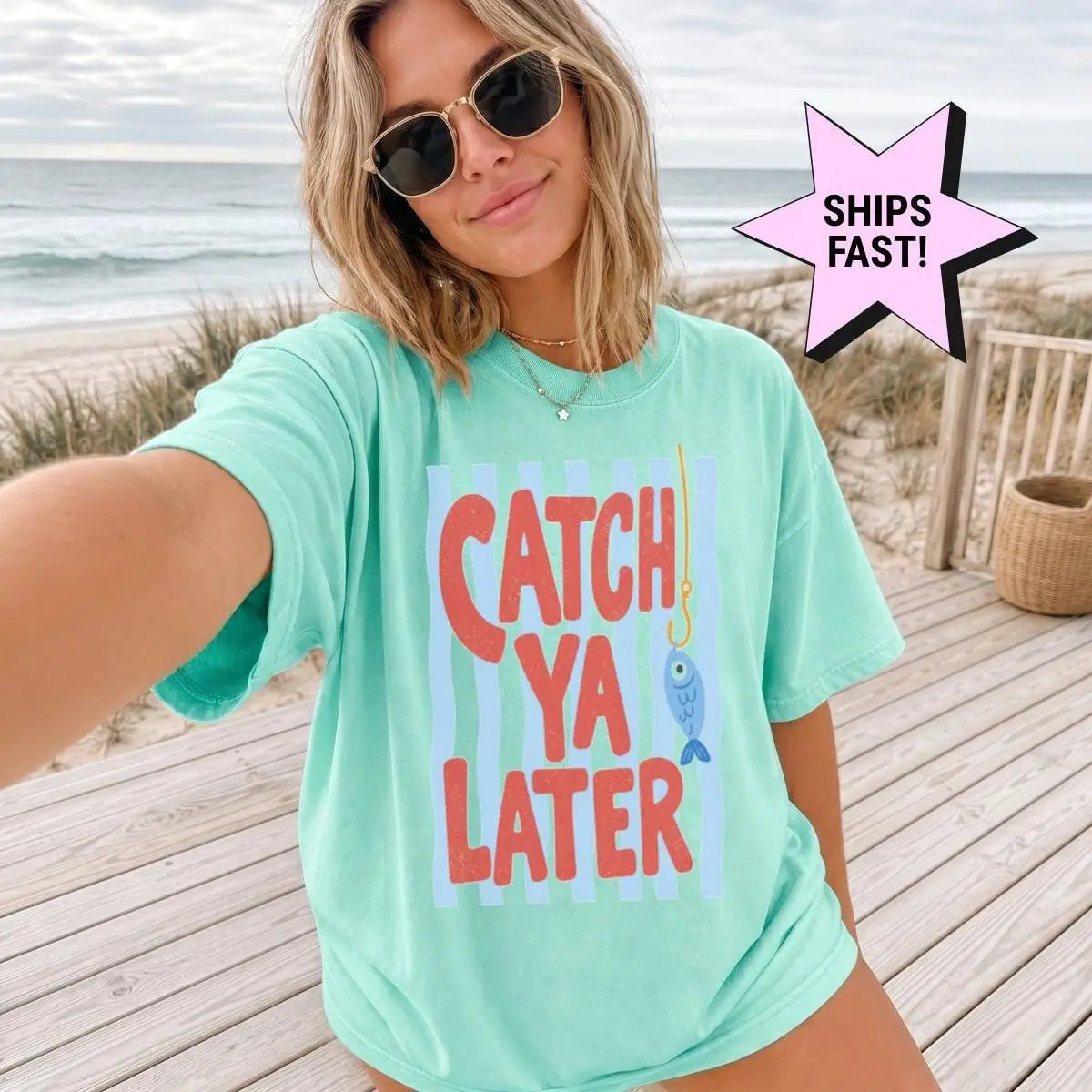 Woman in a Seafoam Comfort Colors tee taking a beach selfie in sunglasses, catch ya later in red on blue stripes