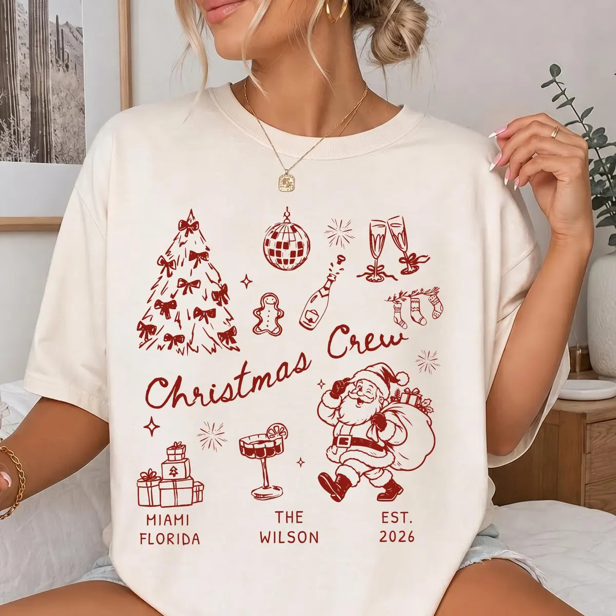 Woman in an Ivory Comfort Colors tee with crimson christmas crew script, bow tree, gingerbread man, cocktail and retro santa