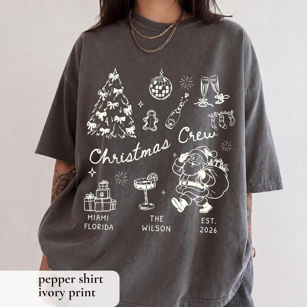 Woman in a Pepper Comfort Colors tee with ivory christmas crew script, bow tree, disco ball, santa and a family name line
