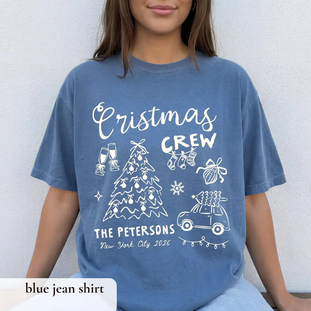 Woman in a Blue Jean Comfort Colors tee seated against a white wall, white crew script tree, car and The Petersons