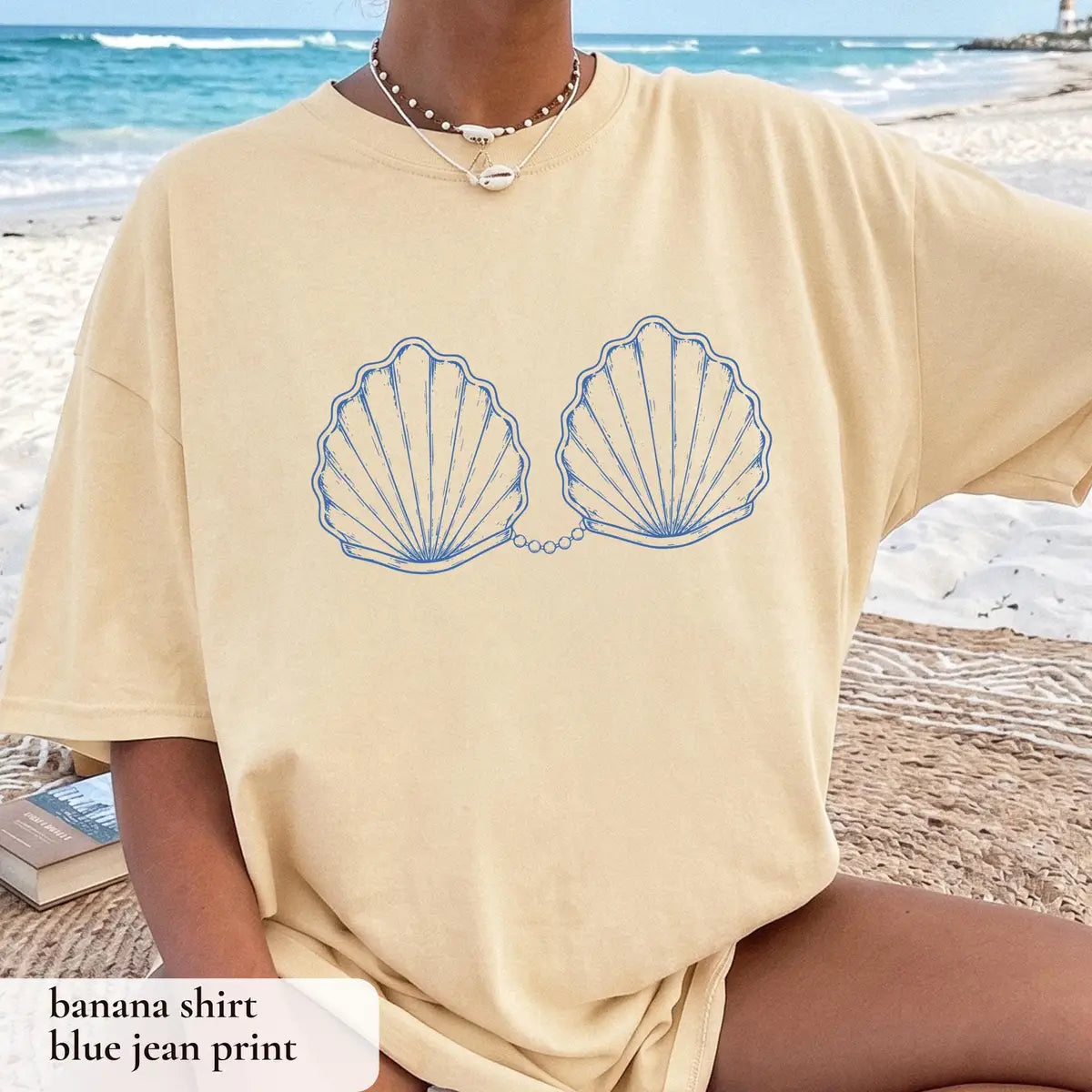Woman in a Banana yellow Comfort Colors tee on a beach, blue outlined scallop shells joined by a pearl chain