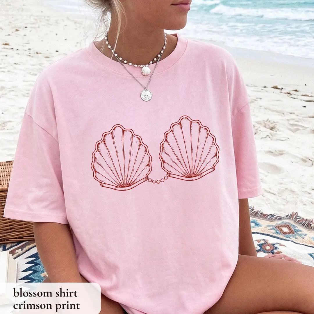 Woman in a Blossom pink Comfort Colors tee by the surf, crimson outlined scallop shells joined by a pearl chain