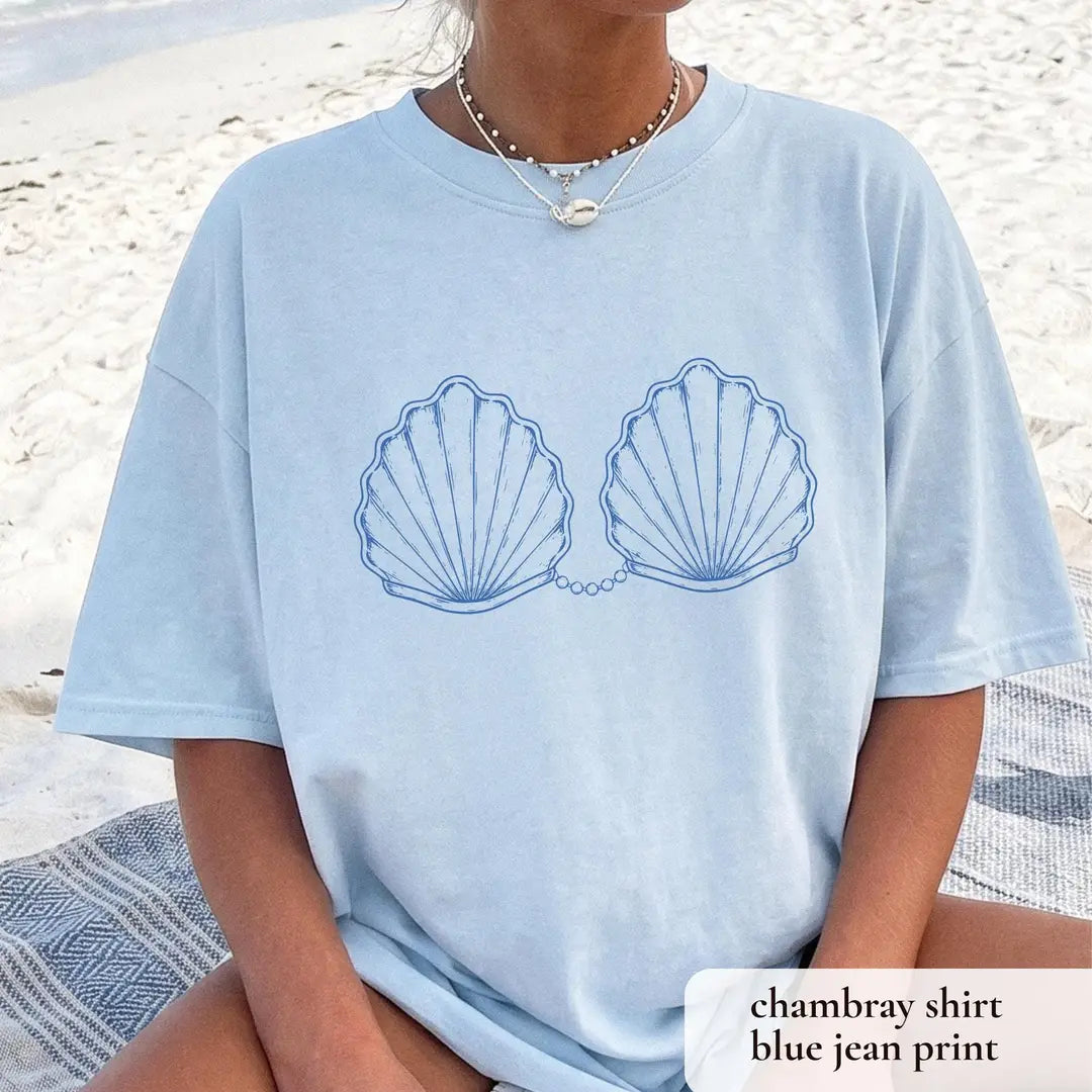 Woman in a Chambray blue Comfort Colors tee on a beach blanket, blue outlined scallop shells and a pearl chain