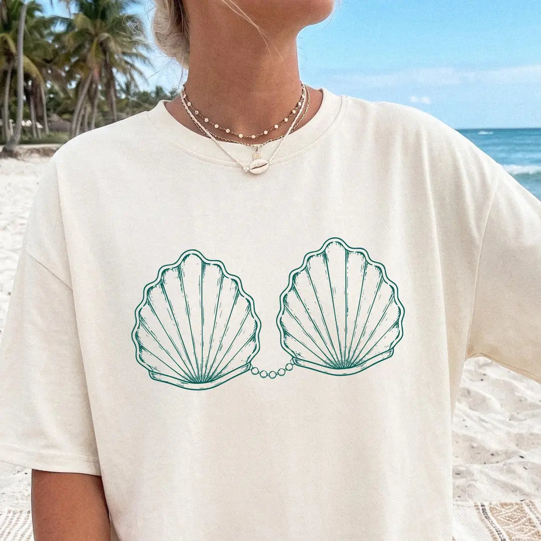 Woman in an Ivory Comfort Colors tee and a pearl necklace, teal outlined scallop shells with a pearl chain on the chest