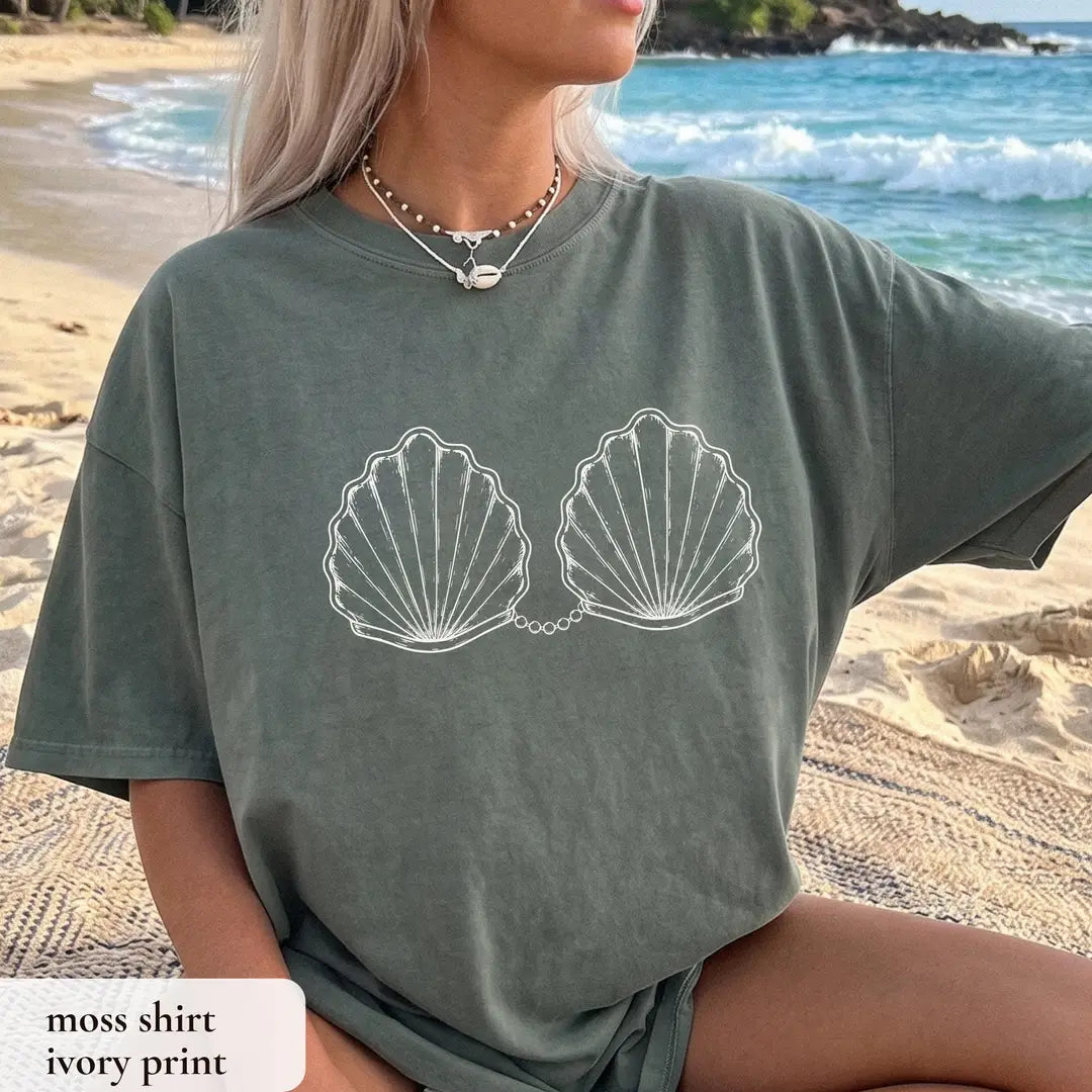 Woman in a Moss green Comfort Colors tee by the waves, white outlined scallop shells with a pearl chain