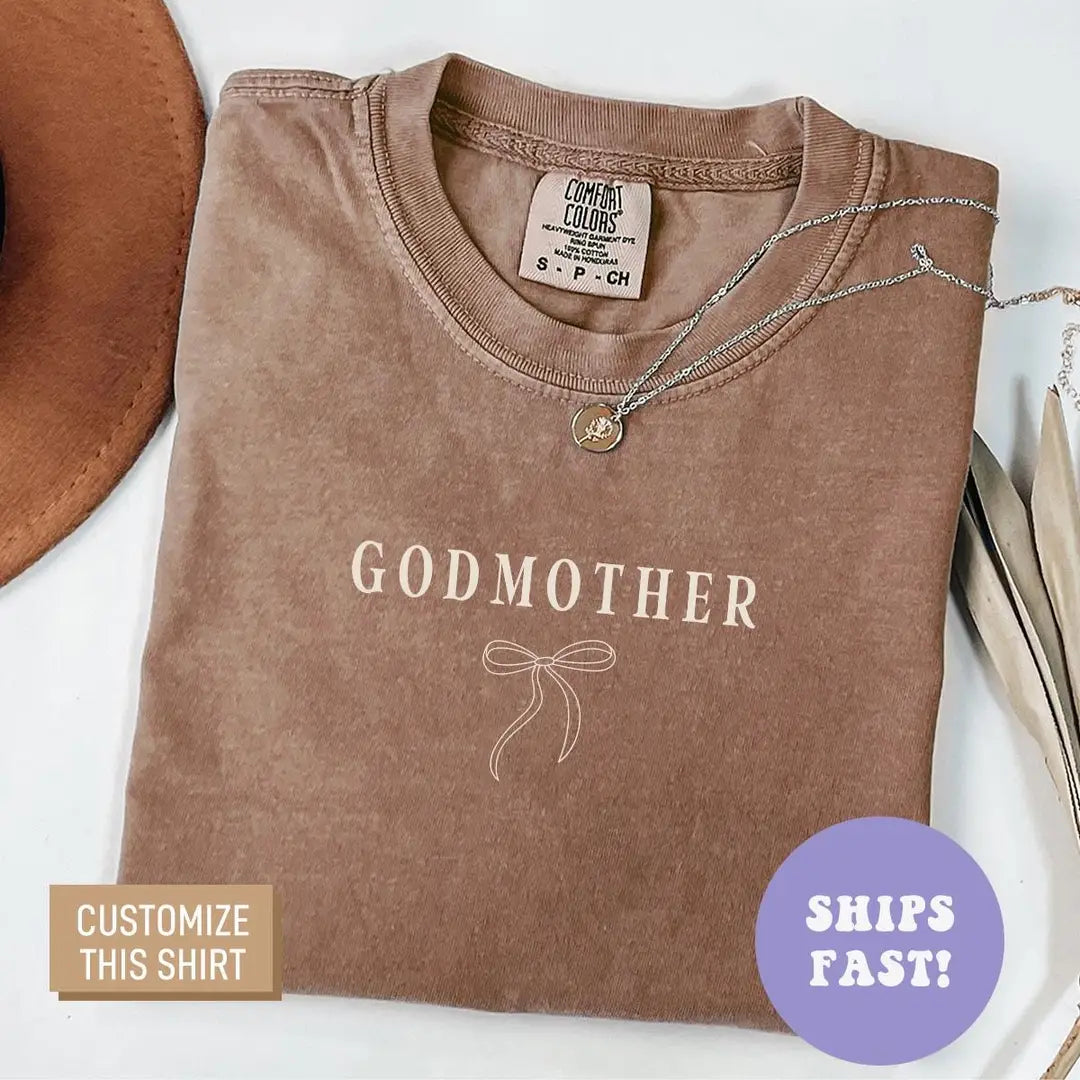 Folded Espresso brown Comfort Colors tee with Godmother in light serif letters above a delicate line-art bow