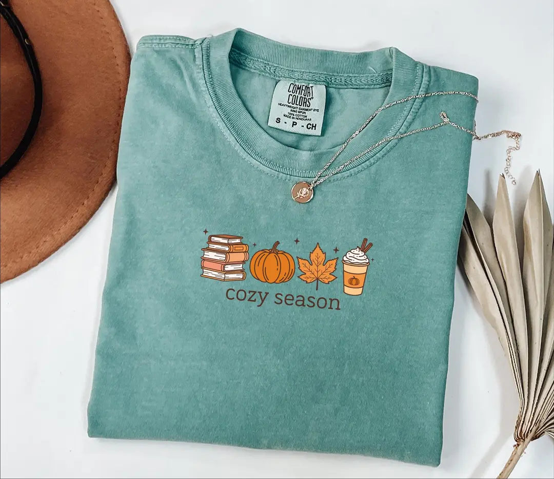Seafoam Comfort Colors 1717 tee with books, pumpkins, a fall leaf, a coffee cup and Cozy Season lettering.