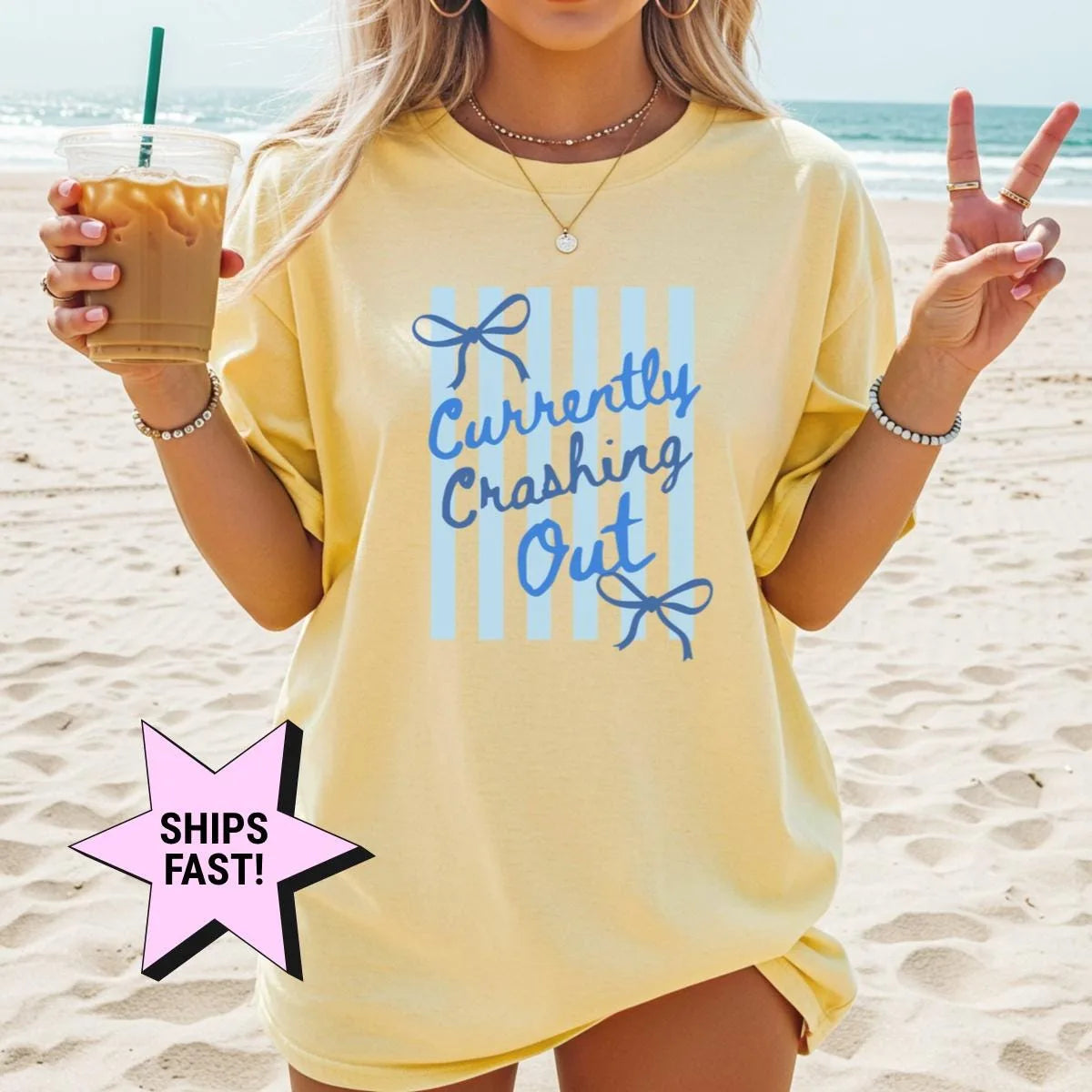 Woman in a Butter yellow Comfort Colors tee on a beach with an iced coffee, blue currently crashing out text on stripes