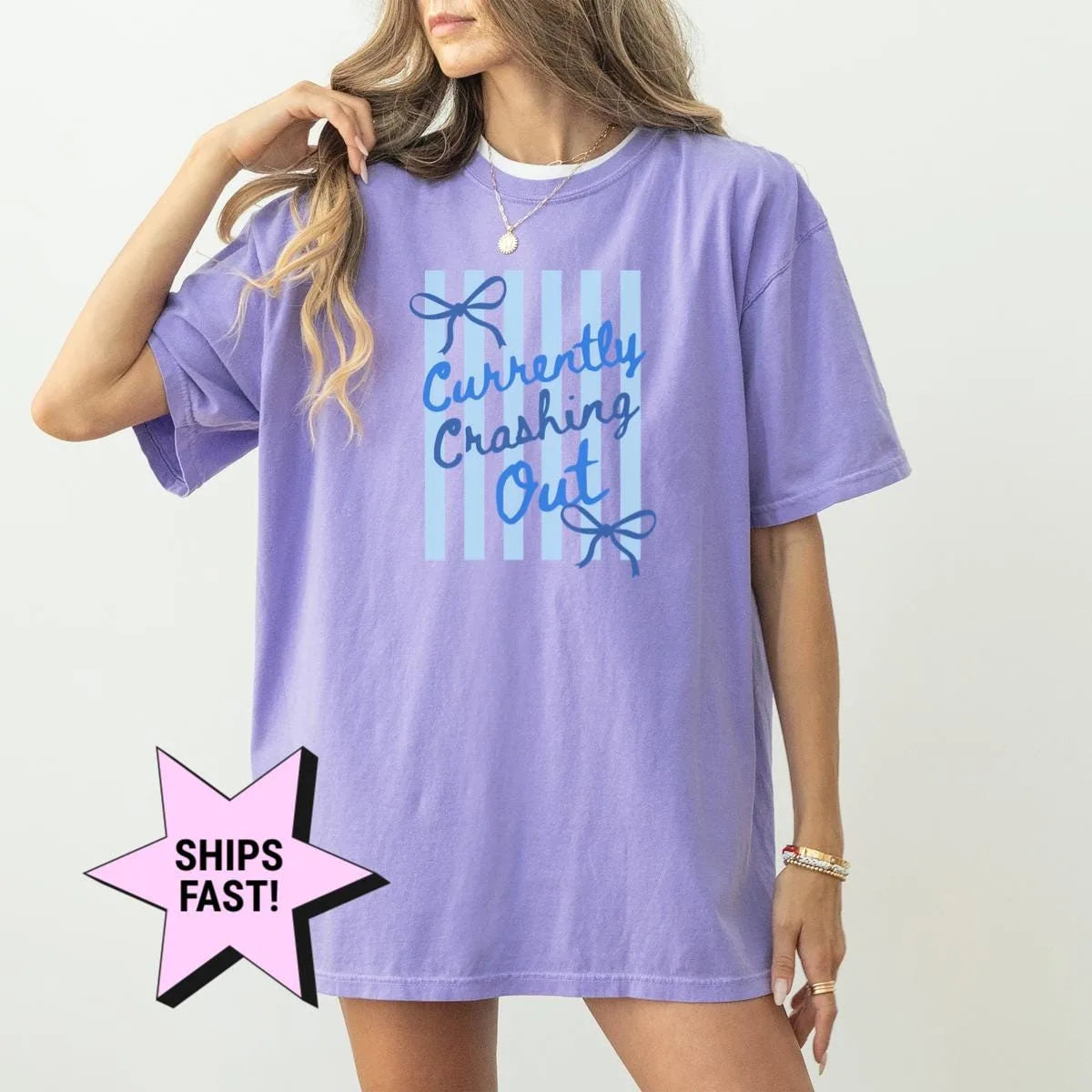 Woman in a Violet Comfort Colors tee, hand in her hair, with blue cursive currently crashing out and bows on blue stripes