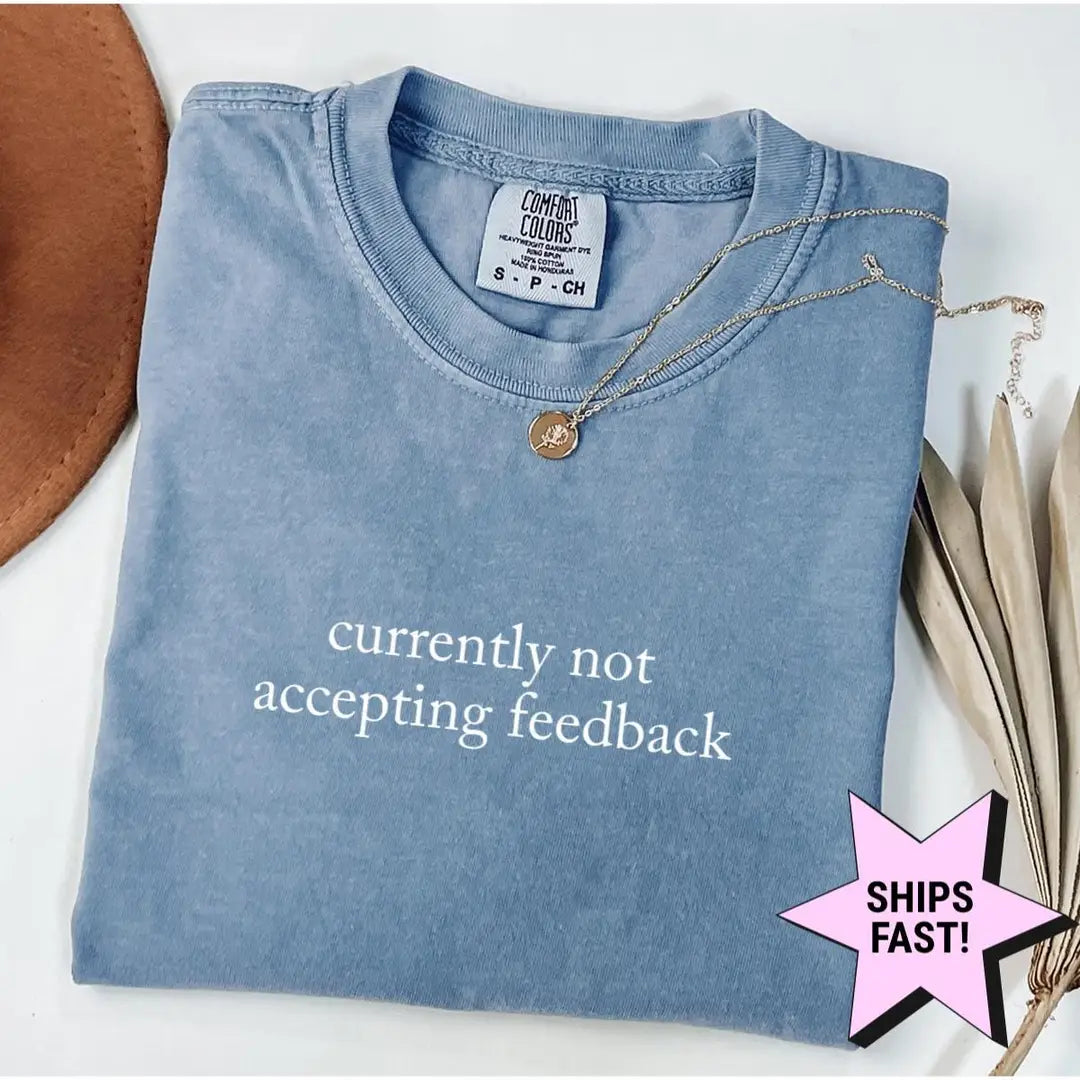 Folded Blue Jean Comfort Colors tee with currently not accepting feedback in white serif type, styled with a necklace