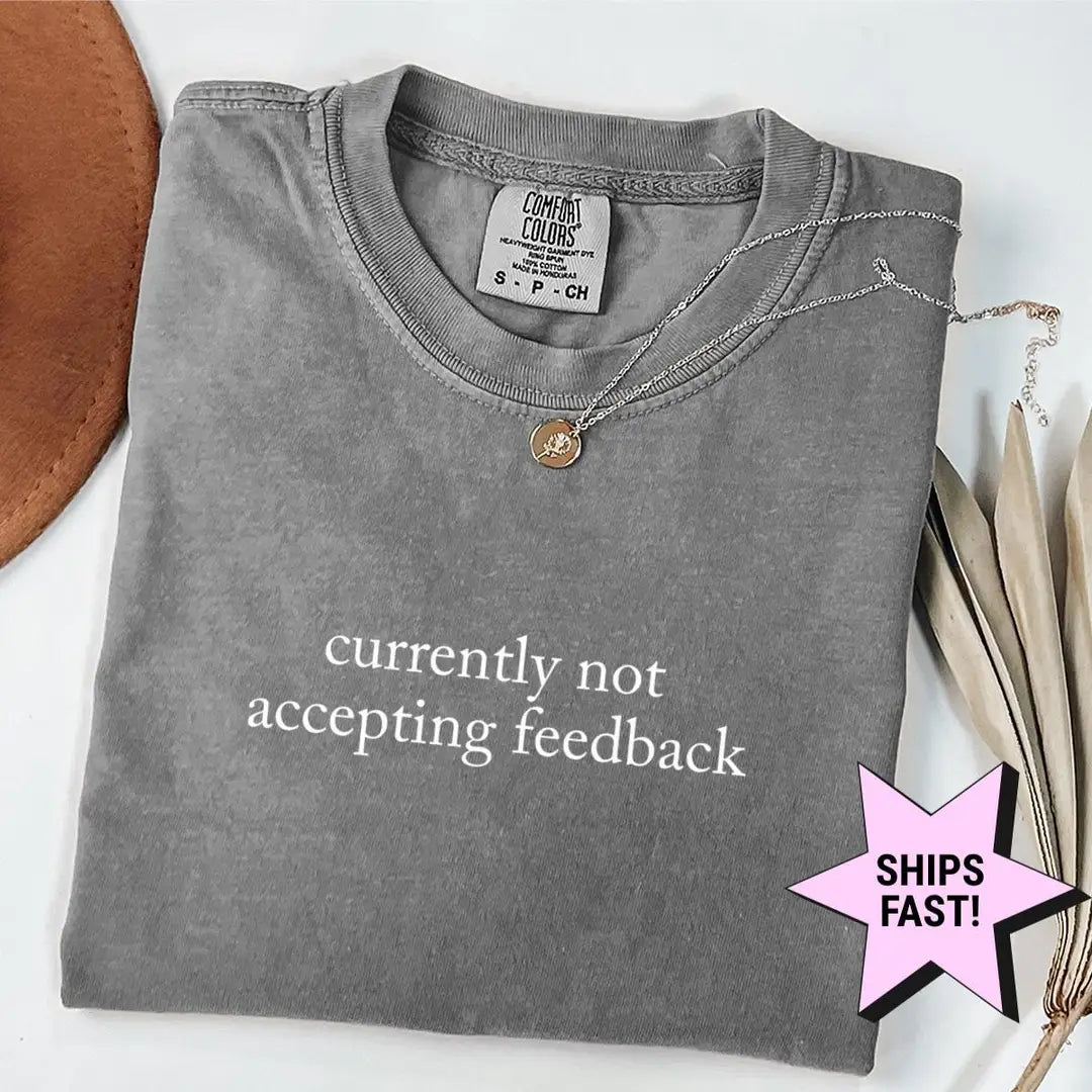 Folded Pepper Comfort Colors tee with currently not accepting feedback in white serif type, a necklace on the collar