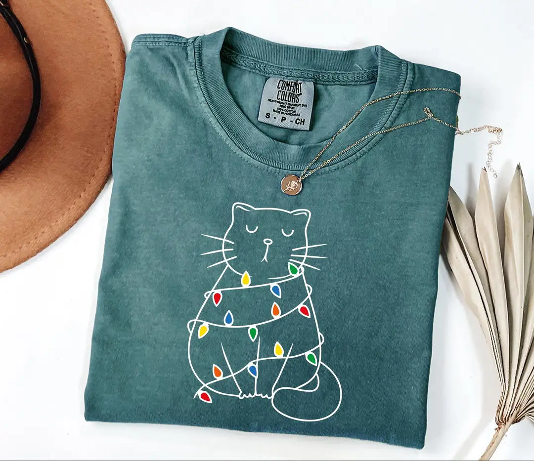 Blue Spruce Comfort Colors T-shirt with a white cat tangled in colorful Christmas lights.