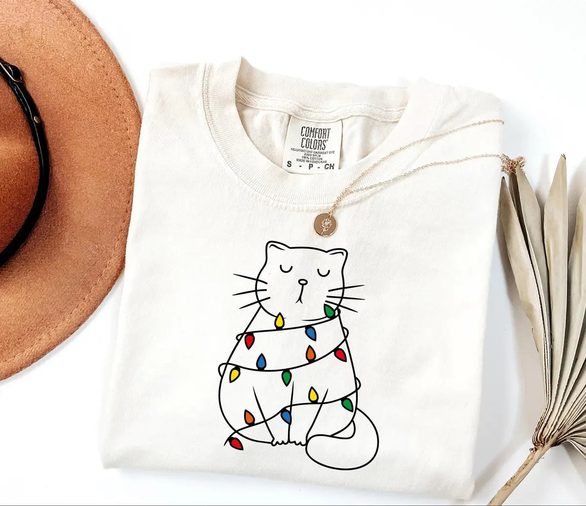 Ivory Comfort Colors 1717 T-shirt with a minimalist cat wrapped in colorful Christmas lights.
