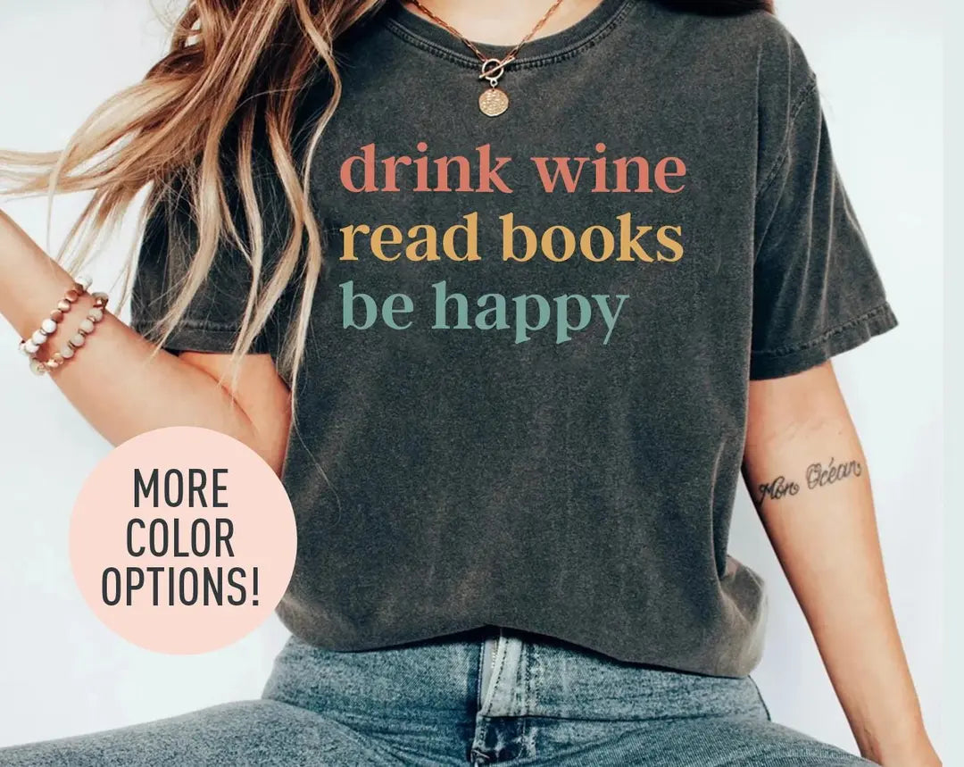 Woman in a dark gray Comfort Colors tee and jeans, bracelets, with drink wine, read books, be happy in three lines