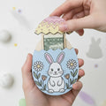 Hand holding a decorative Easter egg-shaped money holder with a rabbit design.