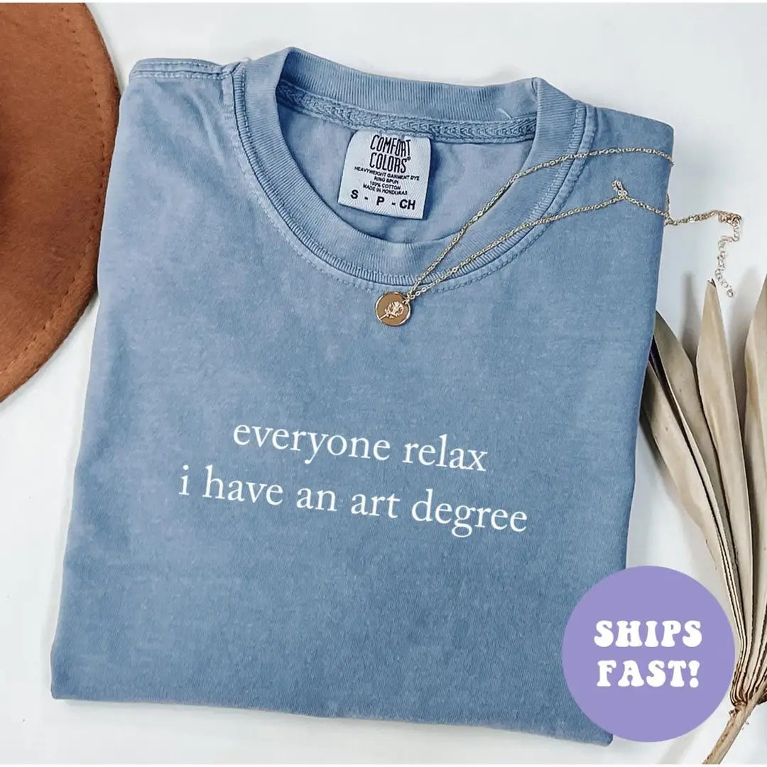 Folded Blue Jean Comfort Colors tee with the two-line art degree quote in white serif, necklace on the collar