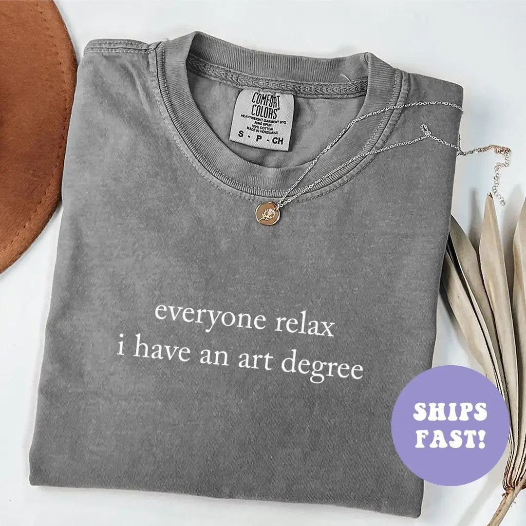 Folded Pepper Comfort Colors tee with everyone relax i have an art degree in white serif, brown hat beside it