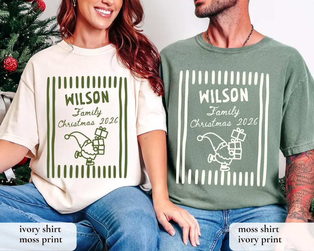 Woman and man on a couch in Ivory and Moss Comfort Colors tees, green Wilson Family Christmas 2026 frame with a gnome