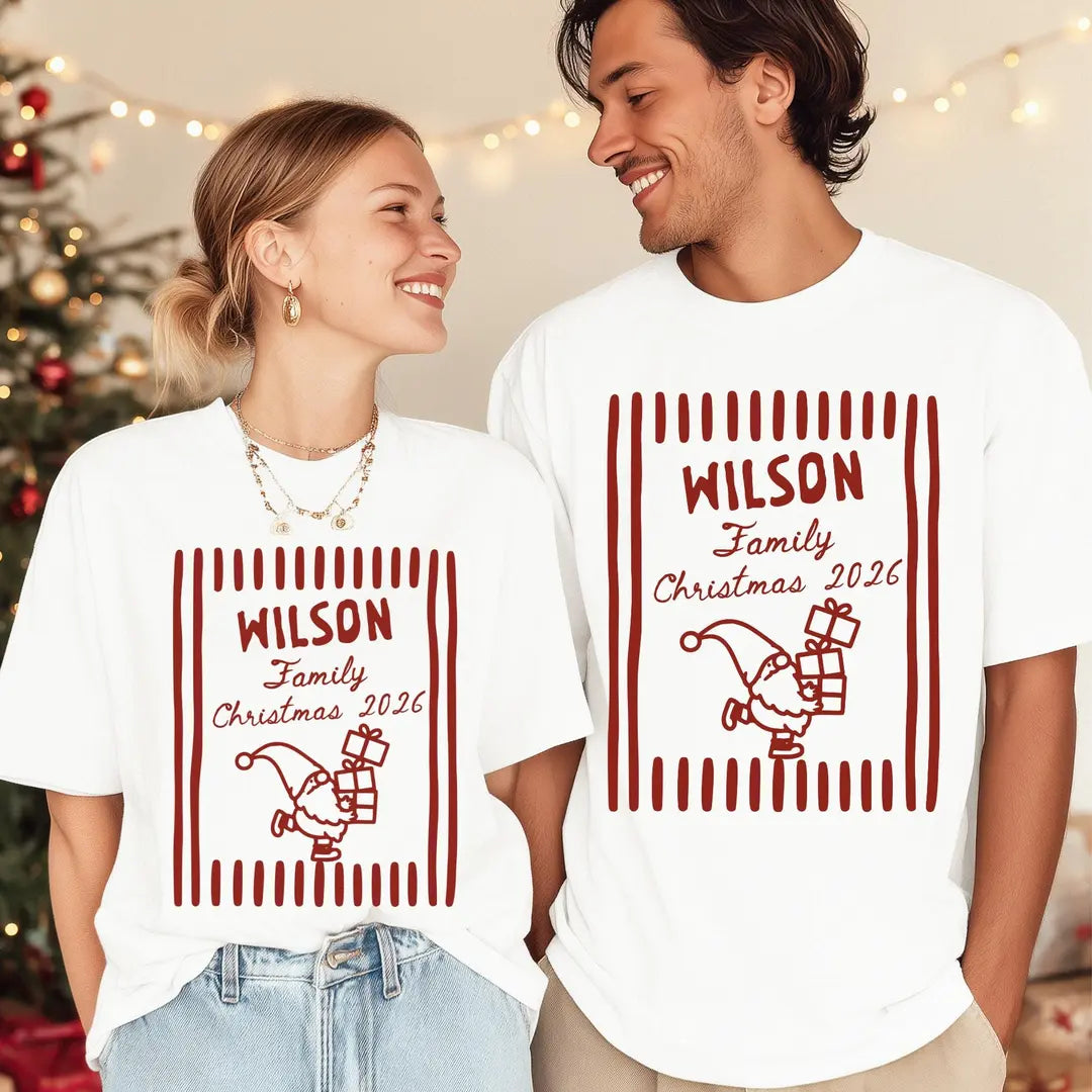 Woman and man in White Comfort Colors tees by a christmas tree with lights, red Wilson Family Christmas 2026 frame and gnome