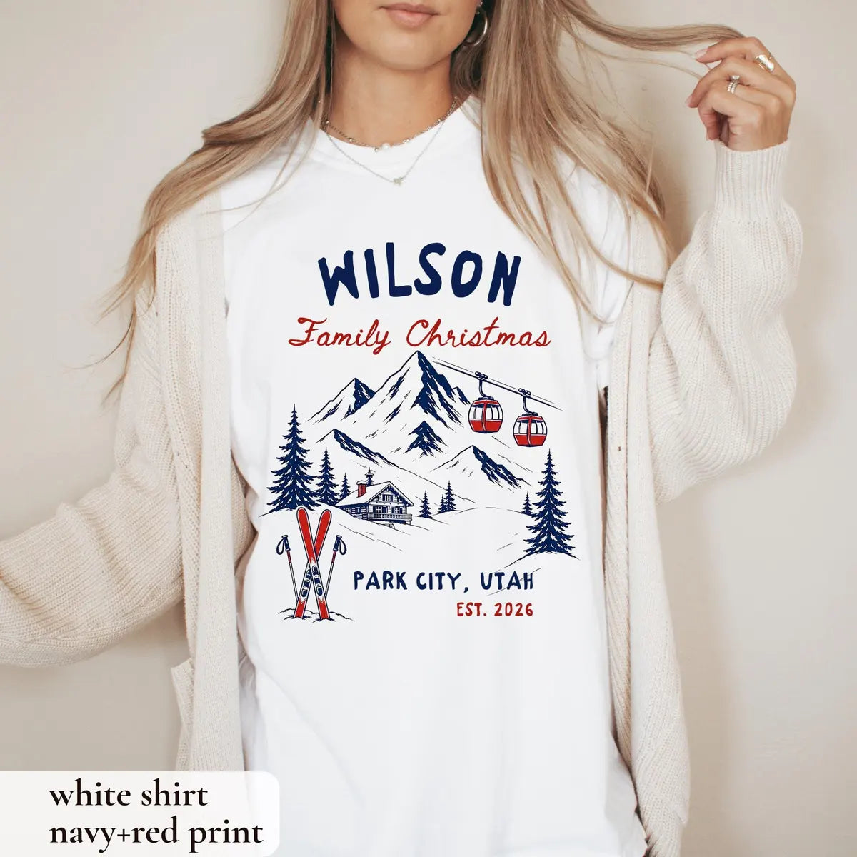 Woman in a White Comfort Colors tee and a cream cardigan, navy Wilson Family Christmas with a mountain, gondolas and skis