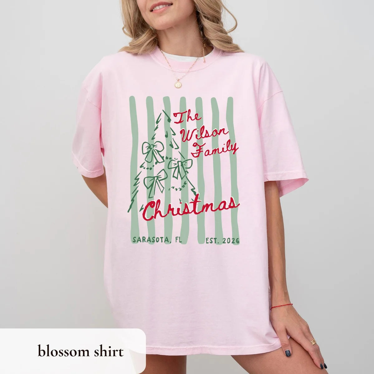 Woman in a Blossom pink Comfort Colors tee, red The Wilson Family Christmas with a bow-covered tree on green stripes