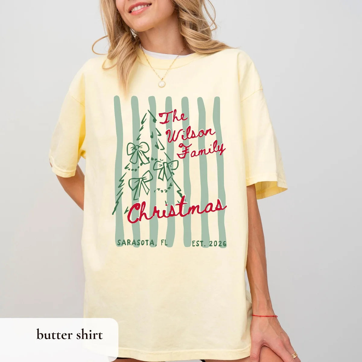 Woman in a Butter yellow Comfort Colors tee, red The Wilson Family Christmas script beside a bow tree and green stripes